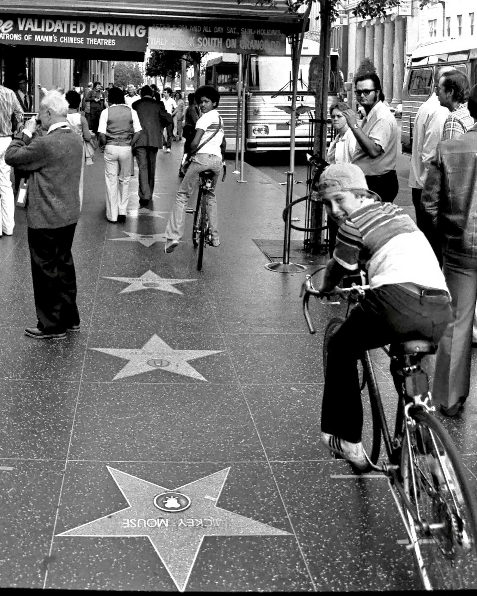Boy on a bicycle pauses on Hollywood Boulevard near the Mickey Mouse star, B&W.