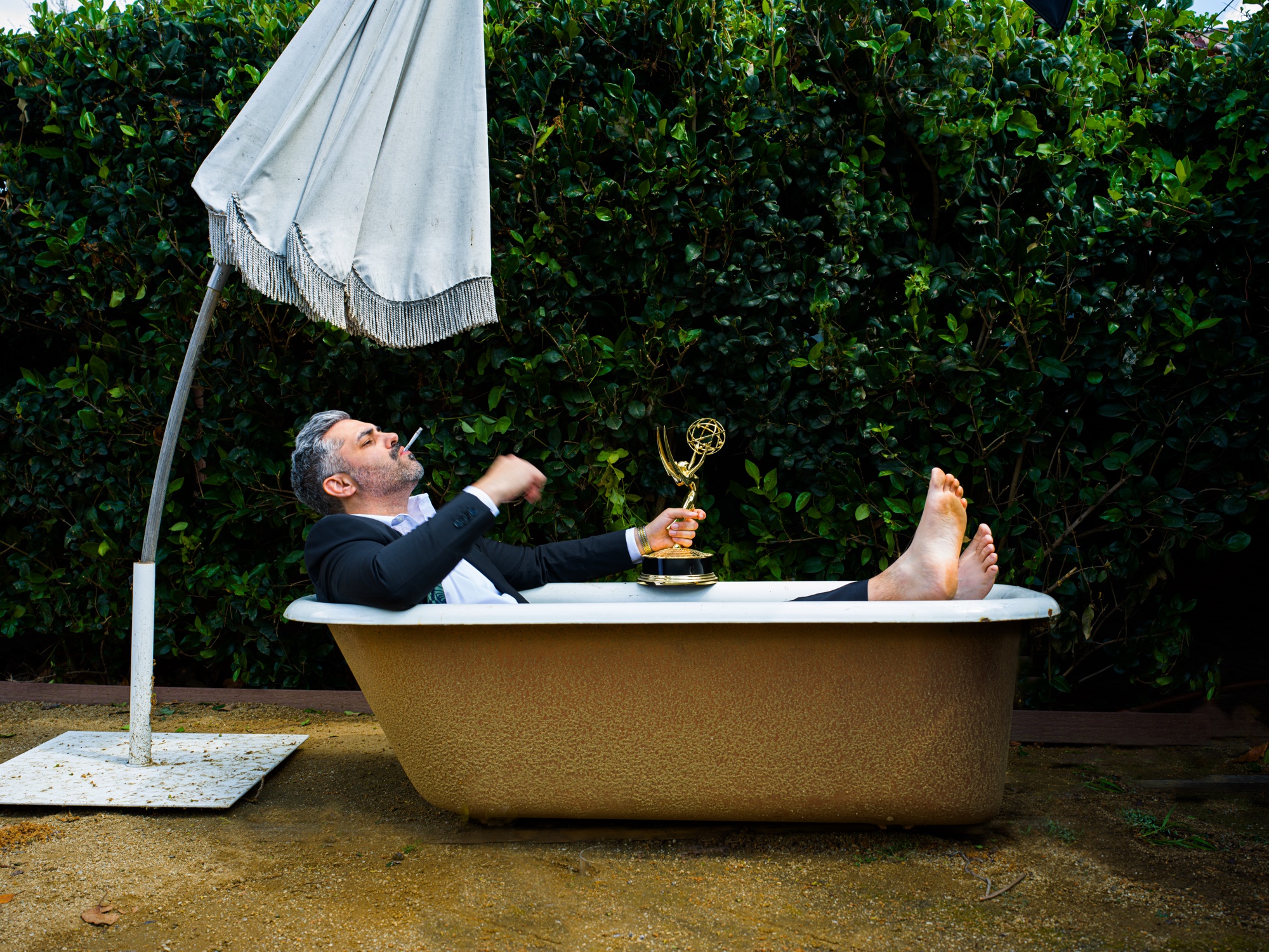 Norm Sousa reclines in a backyard tin bath holding an Emmy, photographed by G. John Slagle.