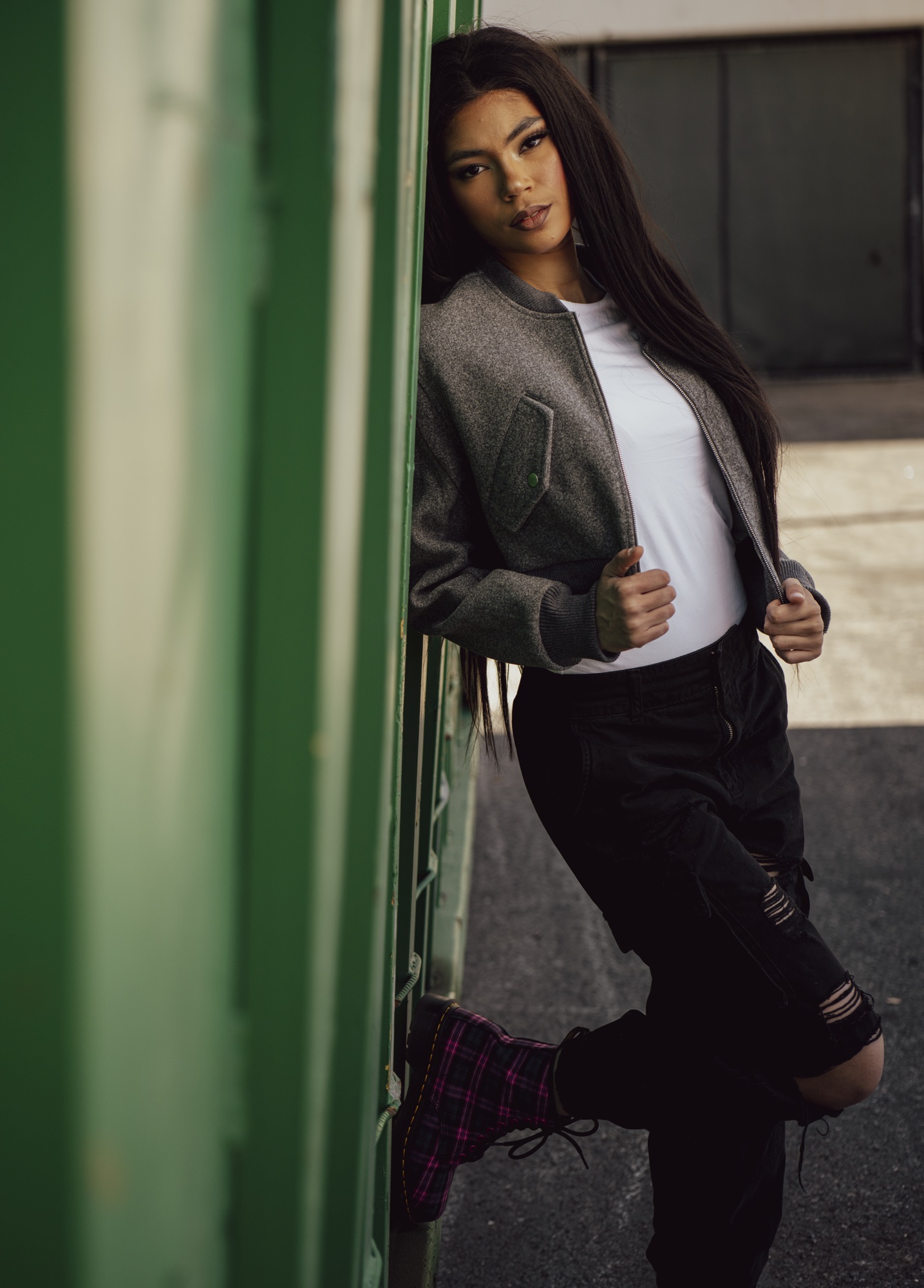 Fashion portrait of model leaning against green corrugated wall.