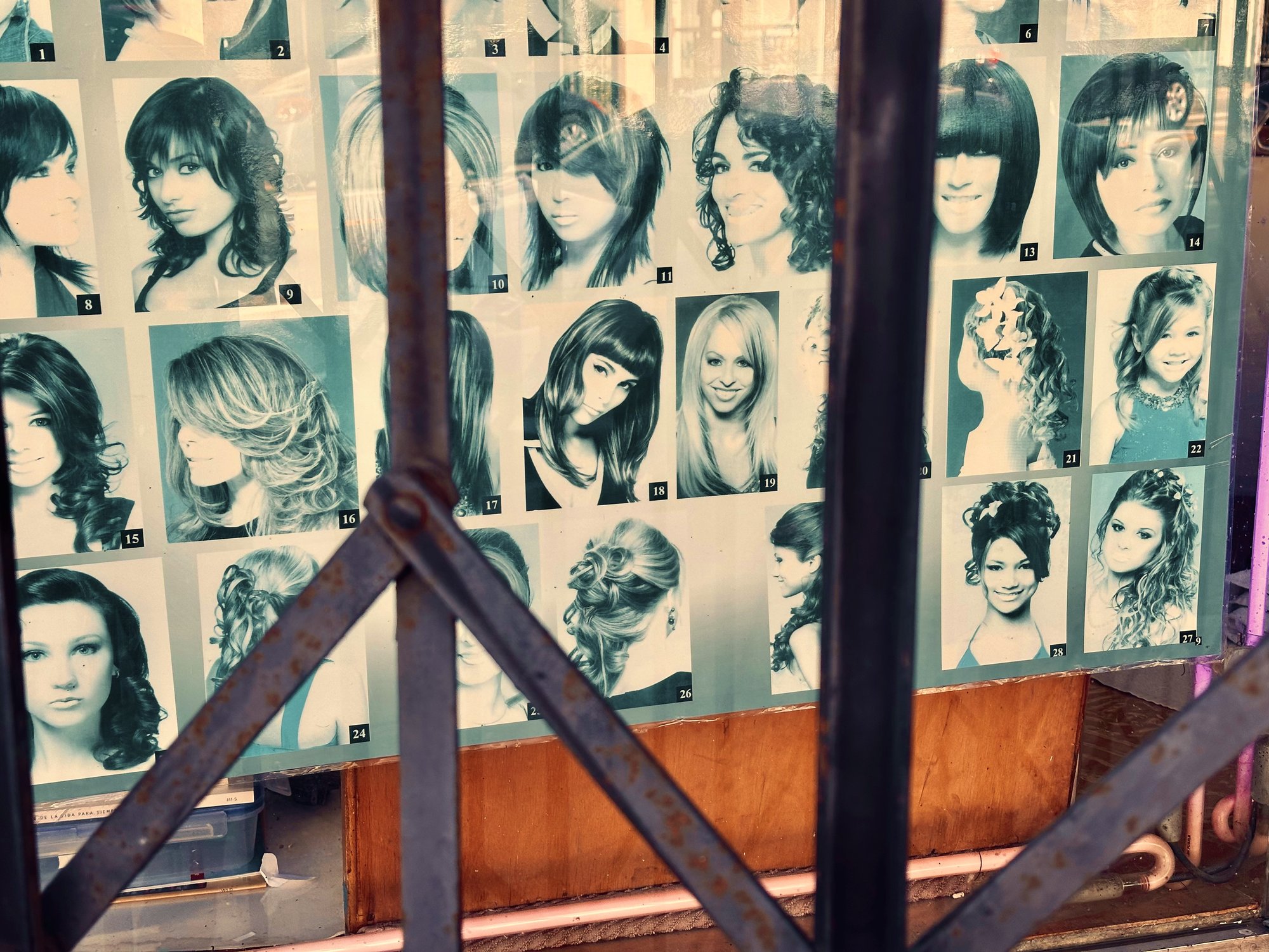 Faded salon poster of women's hairstyles behind a rusted iron window grate, San Pedro, CA.